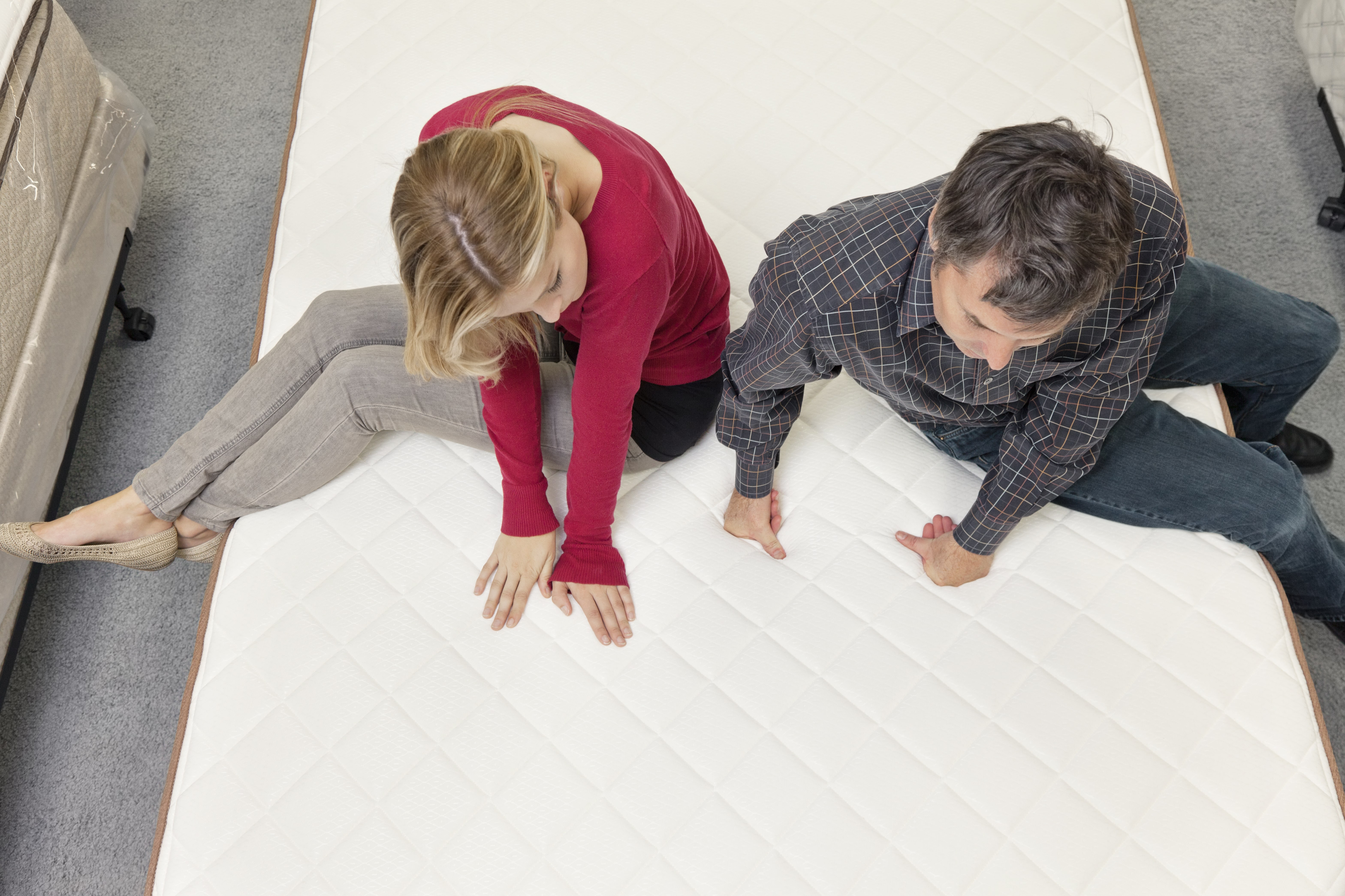 An aerial view of a couple sitting on a foam mattress, trying to decide between foam vs spring mattresses.