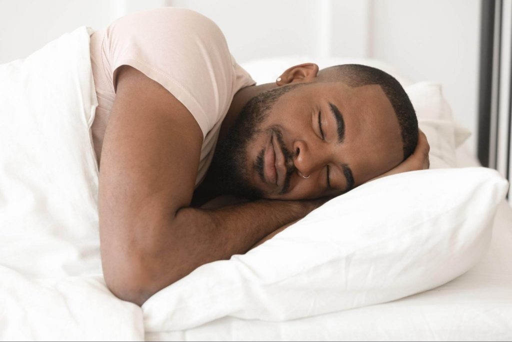 A smiling black man is sleeping on a mattress.