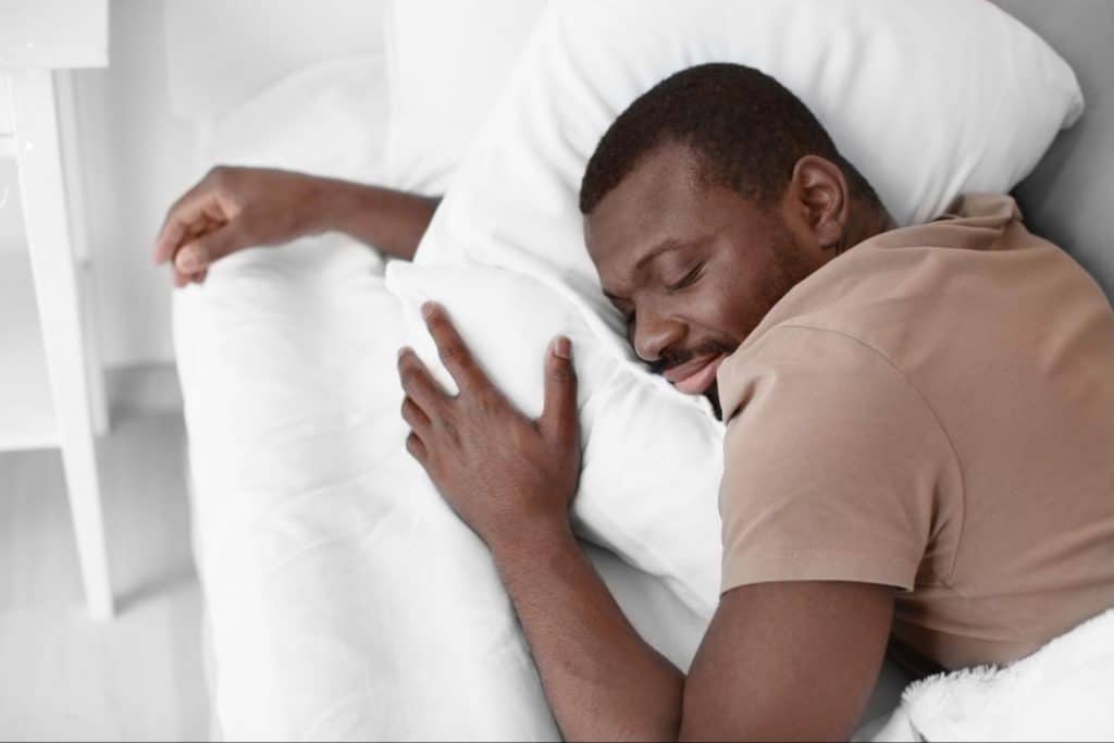 A black man sleeps soundly on a comfortable mattress.
