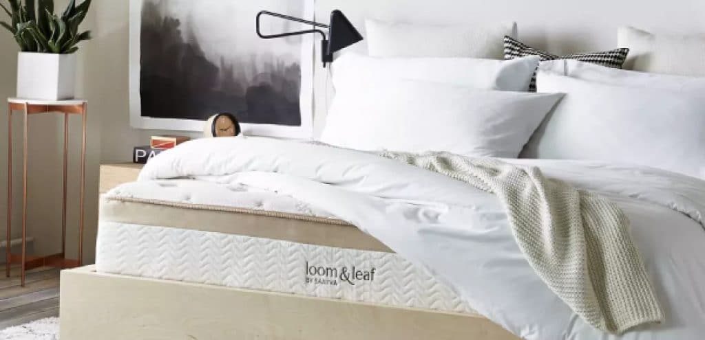 A Loom & Leaf mattress with sheets draped over it in a bedroom.