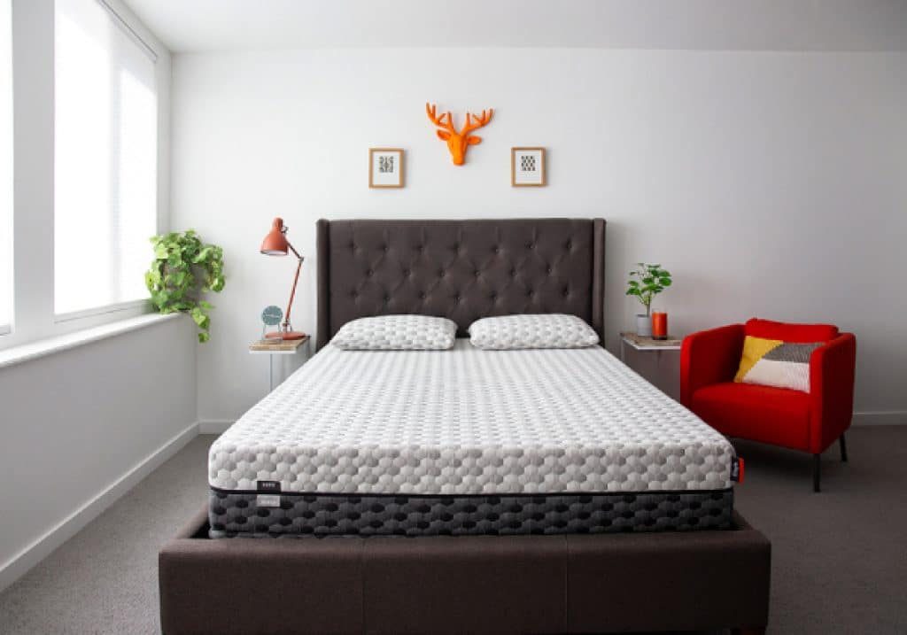 View of a fibromyalgia Layla hybrid mattress on a dark bed frame, viewed from the foot of the bed.