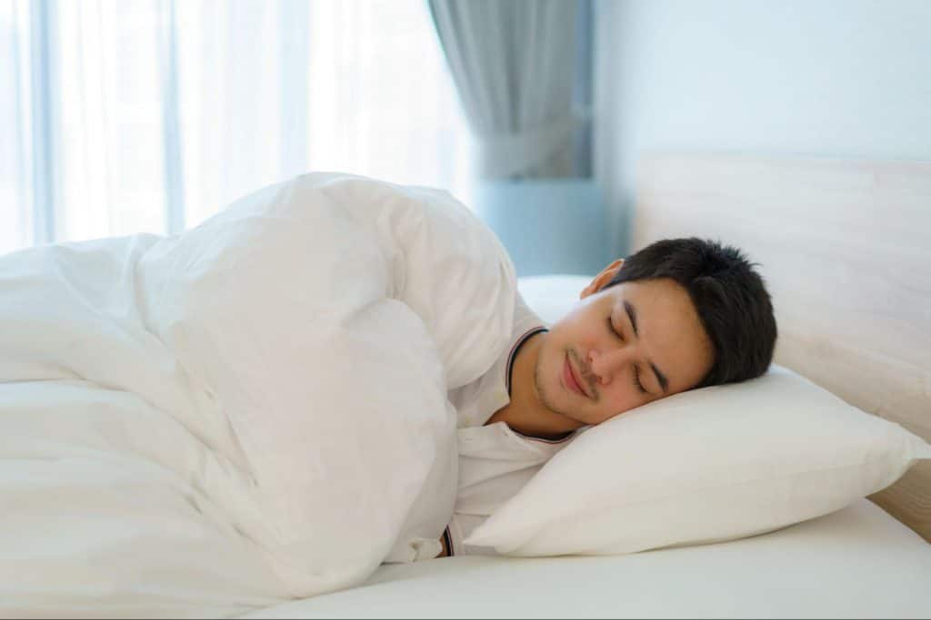 A young man sleeps comfortably on a white mattress.