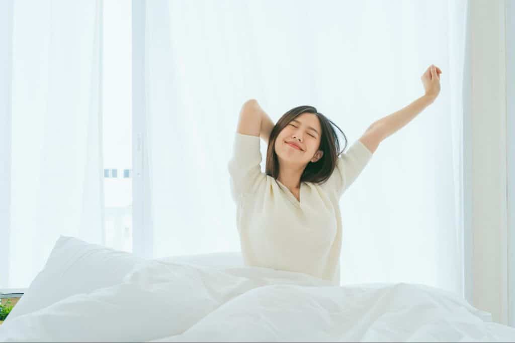 An Asian woman wakes up and stretches, feeling refreshed and pain-free.